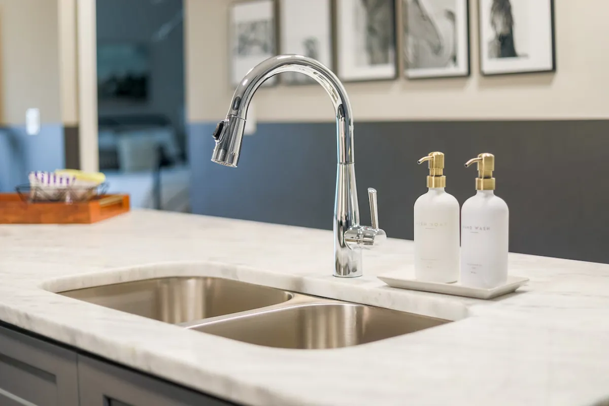 A modern kitchen with a sleek faucet, marble countertop, elegant soap dispensers, and framed artwork. The space is bright and inviting, ideal for family meal prep and social gatherings.