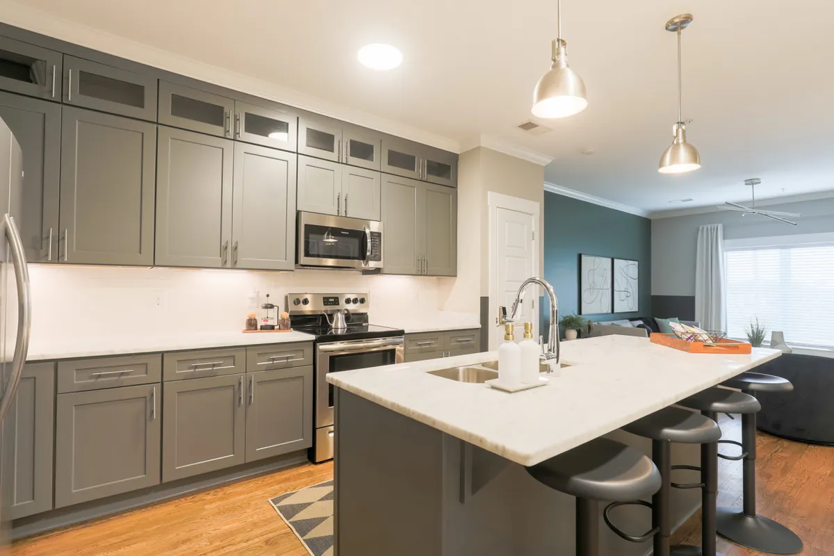 A modern, warmly lit kitchen with a spacious island, stainless steel appliances, marble countertops, and sleek grey cabinetry. The setup is ideal for entertaining, with plenty of space for guests to gather and socialize.