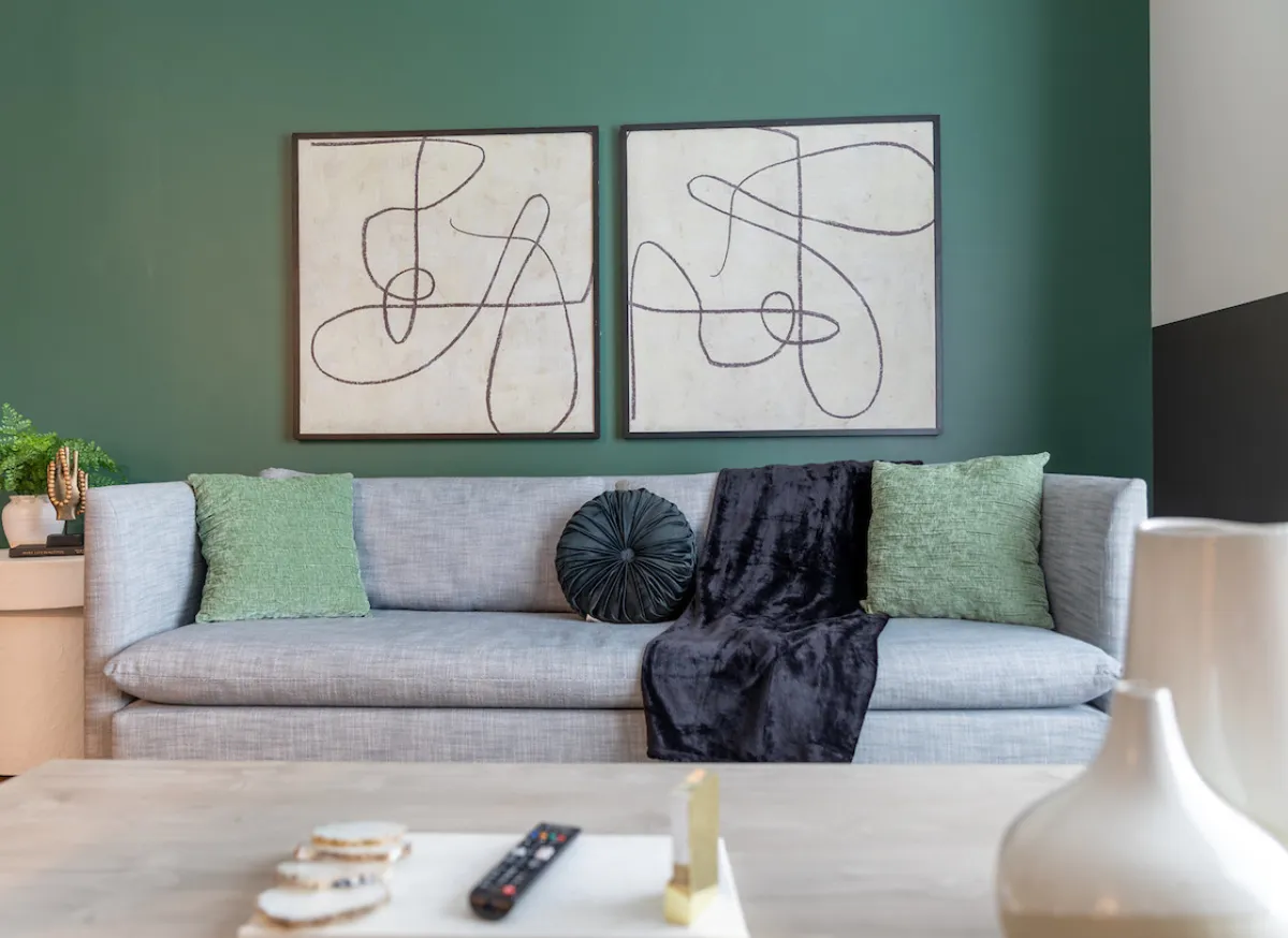A contemporary living space featuring a cozy sofa facing striking abstract artwork and a lush green accent wall. The area feels inviting, perfect for intimate conversations and pre-night-out relaxation.