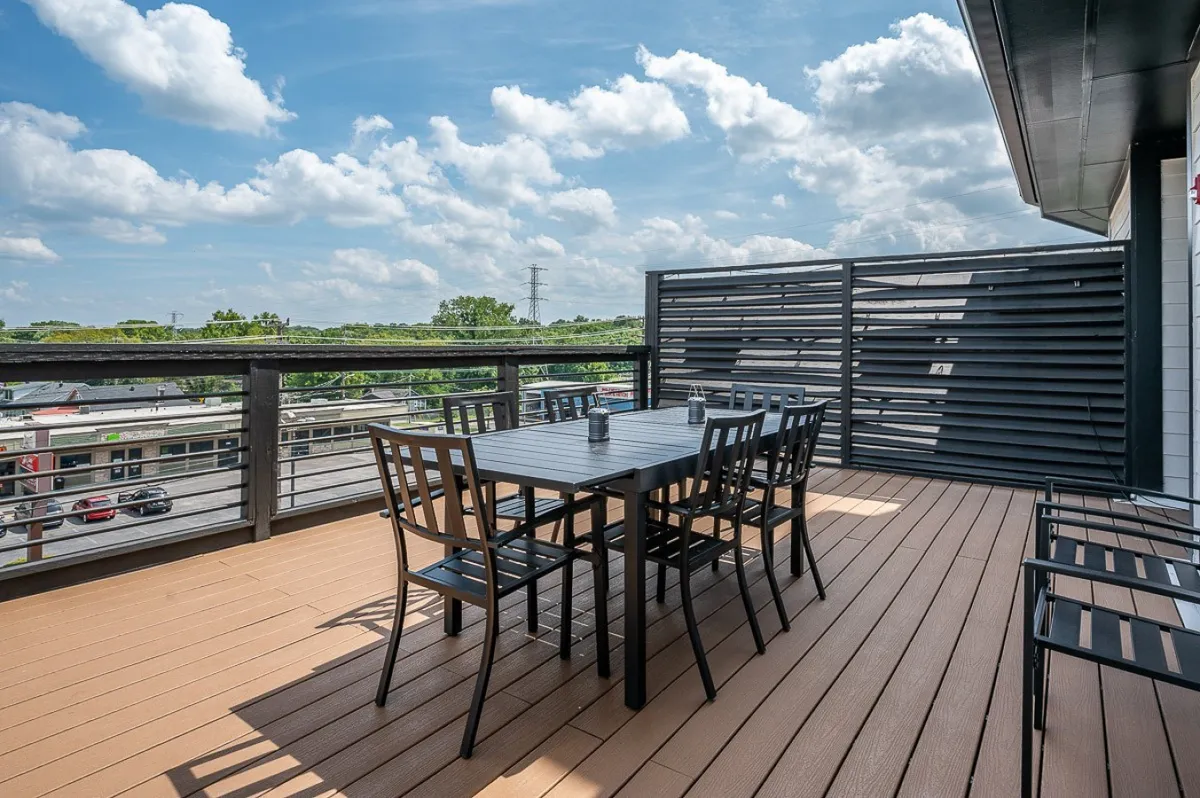 An exterior rooftop space featuring a dining table and chairs set under an open sky, with a backdrop of cityscape and greenery. The ambiance is casual yet elegant, ideal for outdoor dining, entertaining guests, or unwinding with a book.