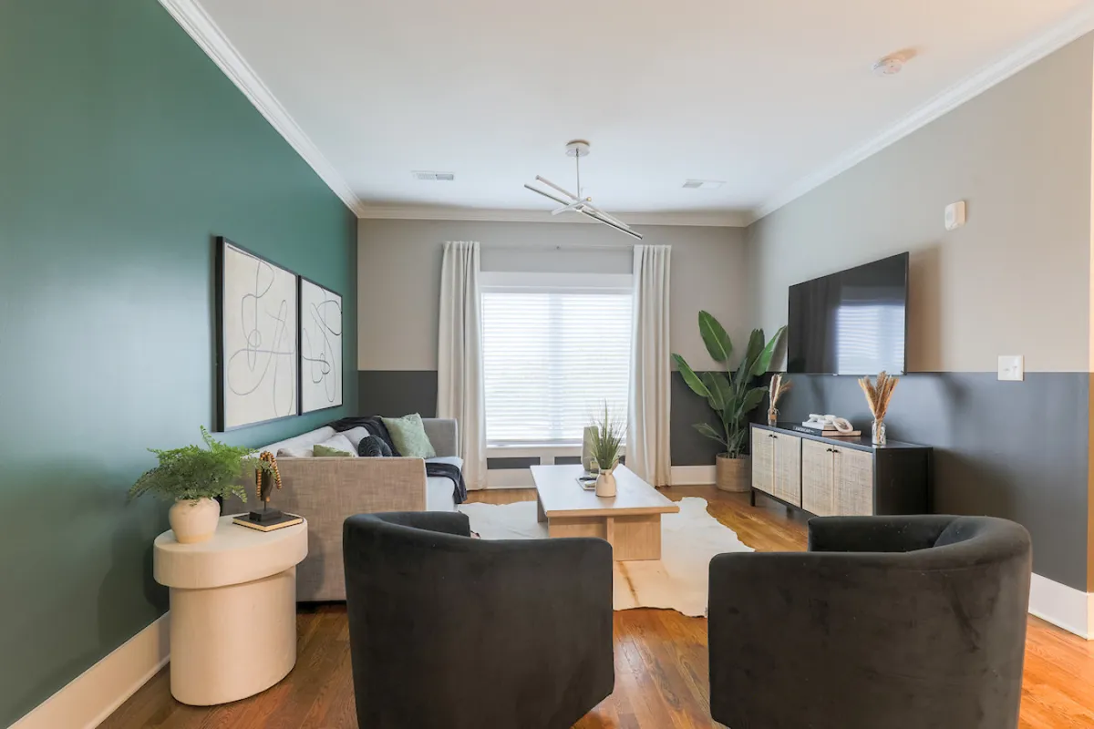 A bright, contemporary interior featuring a green accent wall, stylish furniture, a large window flooding the space with natural light, and a potted plant. While not specifically the entryway, the open layout and visible pathway suggest accessible, barrier-free movement.
